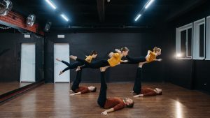 Five dancers showcase flexibility and balance in a dance studio during rehearsal.